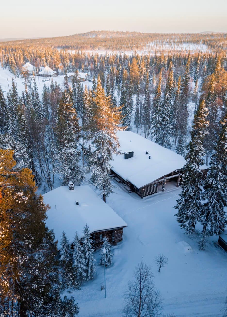 Aerial view of snow-covered log chalets in the forests of Luosto